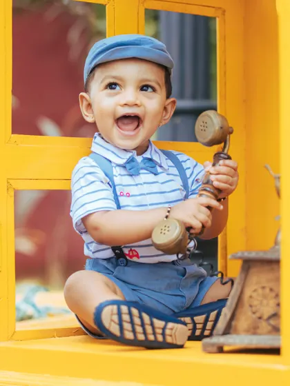 An expressive and joyful shot of a little boy in a bright yellow window, holding a vintage telephone receiver.