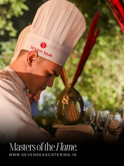 "Masters of the Flame." This graphic captures the focus and precision of our chefs. Here, a chef in a branded "Seven Seas" toque is intently focused on his craft, representing our dedication to culinary mastery.