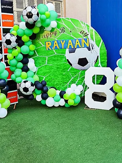 An outdoor football party for an 8th birthday. This setup includes a goal-themed backdrop, balloon columns, and a large light-up number '8'.