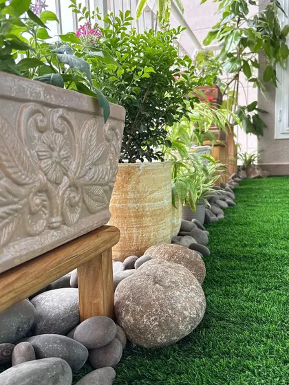 A low-angle view showing the details. The carved planter, smooth river pebbles, and artificial turf create a multi-textured landscape that is interesting and beautiful from every angle.