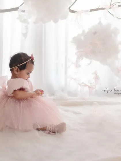 A quiet, contemplative moment during a first birthday shoot. The soft, dreamy setup with fluffy clouds and a simple cake creates a serene and beautiful scene.