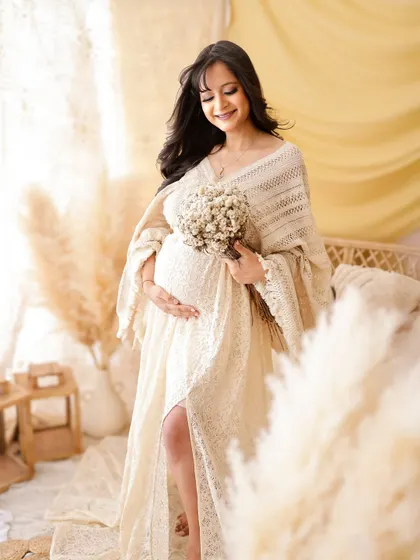 A duplicate of image 2, this dreamy, light-filled portrait captures a mom-to-be in a soft, cream-colored knit dress, surrounded by a boho setup.