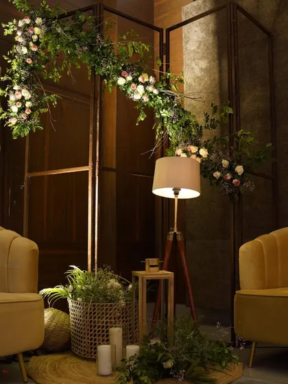 An elegant lounge area with plush yellow armchairs. A floral garland drapes over a modern metal screen, beautifully blending natural and contemporary design elements.