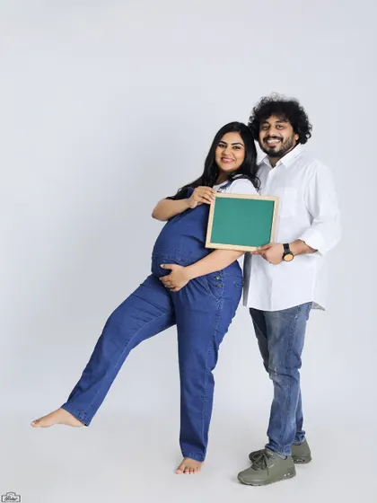 A fun and classic studio portrait of an expecting couple. They hold a blank chalkboard, perfect for adding a personalized message or due date announcement.
