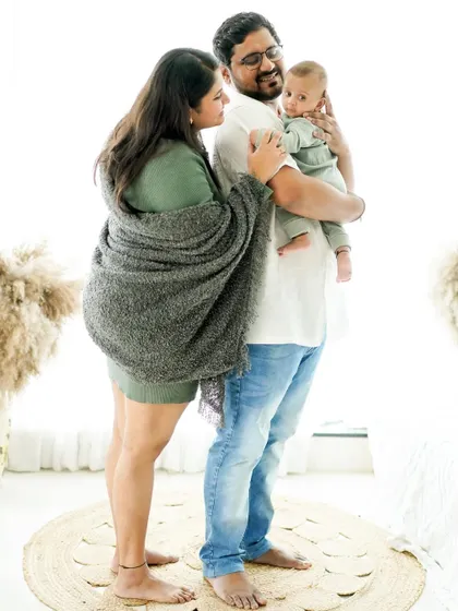 A full-length family portrait from a lifestyle newborn shoot. The cozy blanket and casual outfits create a feeling of warmth and comfort, just like being at home.