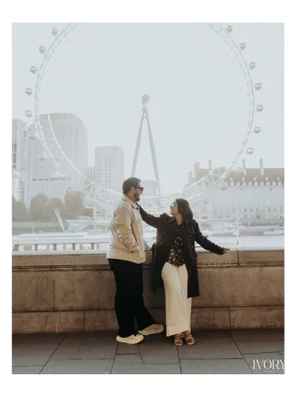 A full-length portrait of the couple sharing a moment in front of the London Eye. The soft, hazy light gives the scene a dreamy quality, perfectly capturing the romance of their destination pre-wedding shoot.