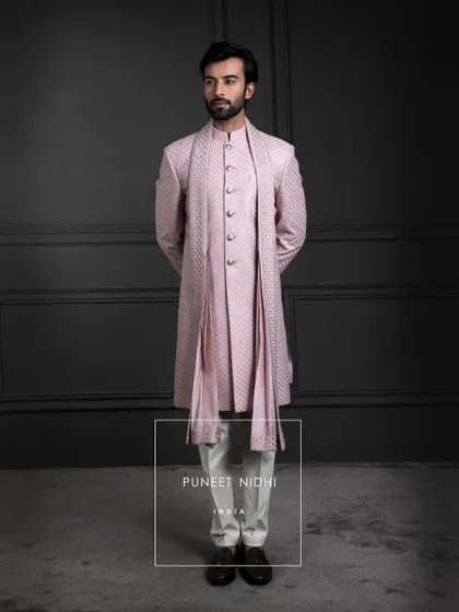 Blush tones meet timeless artistry. A sherwani in pink silk, layered with a fish-scale textured achkan and matching stole, becomes a portrait of soft elegance.