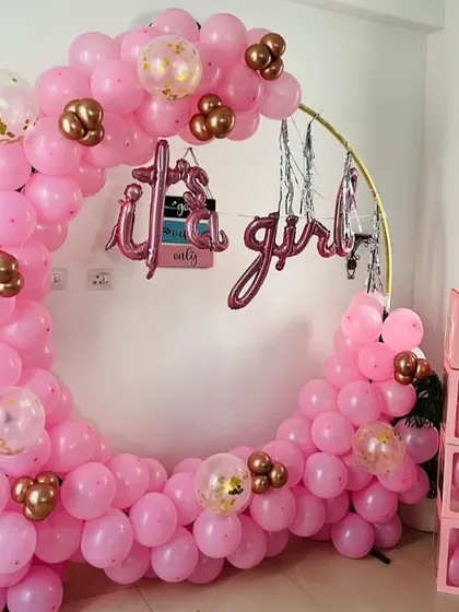 An "It's a Girl" welcome baby decoration with a full ring of pink balloons. The setup also includes pink "BABY" blocks.