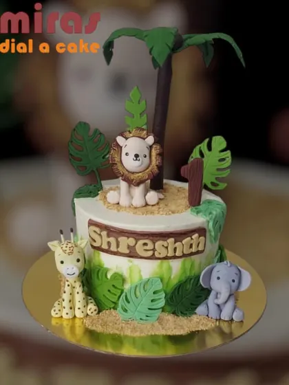 A charming jungle-themed cake for a first birthday. This design features a cute lion, giraffe, and elephant surrounded by fondant leaves and a palm tree, creating a sweet safari scene.