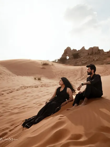 A wide shot showing the couple sitting on a vast sand dune, conveying the scale and solitude of the desert. It's a perfect moment of peace and togetherness.