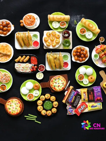 A dark, moody shot of various miniatures, including dosa, pizza, sweets, and chocolates.