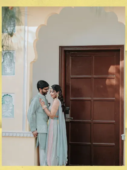 A romantic portrait of the couple by a traditional doorway, a quiet moment amidst the lively Haldi festivities.