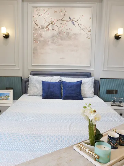 This bedroom design uses a serene color palette of blue and white, with a beautiful cherry blossom artwork above the bed. The wall sconces provide soft, ambient lighting perfect for winding down.