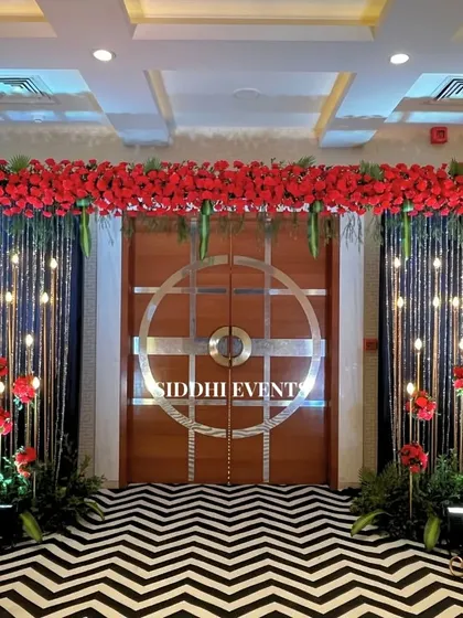 A dramatic entrance with a bold black and white chevron carpet, a canopy of red flowers, and sparkling string lights, perfect for a glamorous evening affair.