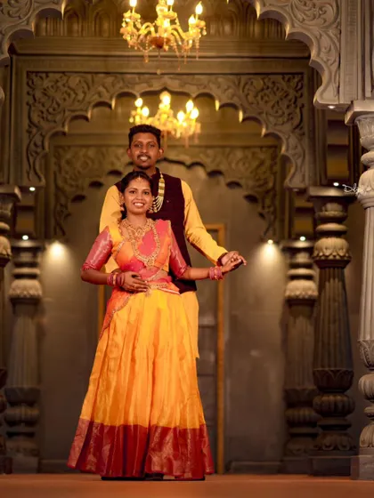 A beautiful indoor pre-wedding photo with the couple in vibrant traditional outfits. The grand setting with pillars and chandeliers adds to the royal feel.