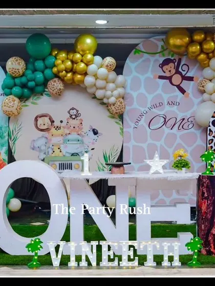 Vineeth's "Wild and One" jungle safari party featured a large "ONE" table and a backdrop with his photo. The setup is filled with cute animal props and earthy-toned balloons.