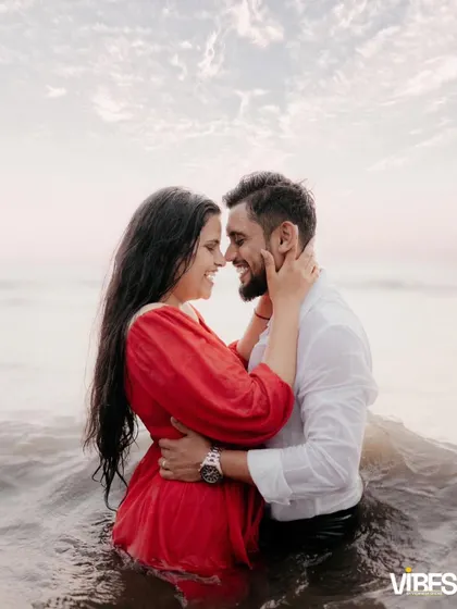 A passionate and joyful photo of a couple embracing in the ocean waves, laughing together. The bride's red dress contrasts beautifully with the water, creating a vibrant and memorable image.