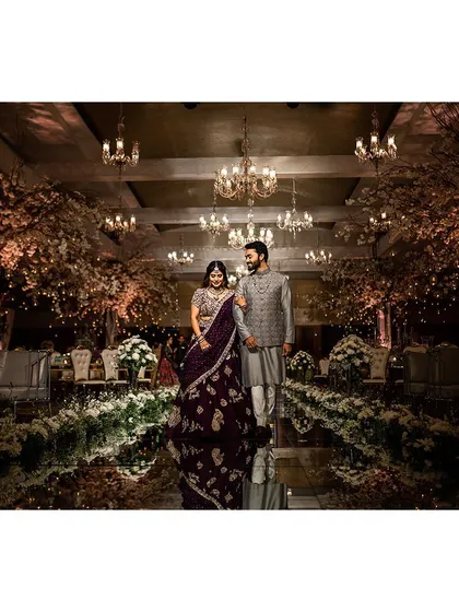 A couple walks down a reflective mirrored aisle, flanked by cherry blossom trees and elegant chandeliers. This setup creates a sophisticated and romantic ambiance, perfect for a grand entrance or a stunning photo opportunity.