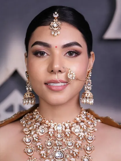 A close-up of a sleek and clean bridal updo, showing how it perfectly frames the face and allows the statement jewelry, like the maang tikka and nath, to shine.