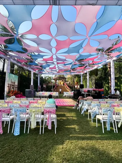 The seating area for a 'Mumbai Fiesta' themed Haldi. The ceiling is a canopy of colorful floral cutouts, and the chairs are decorated with vibrant, patterned ties, creating a lively carnival atmosphere.