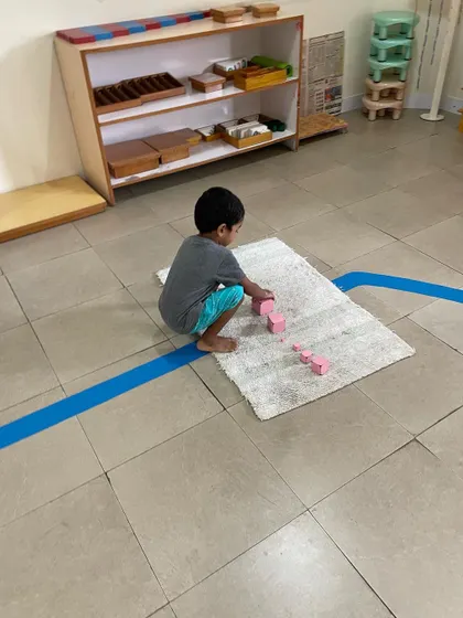 A child works with the Pink Tower, a classic sensorial material. This activity helps them visually discriminate between sizes and builds their understanding of dimensions, which is an indirect preparation for mathematics.