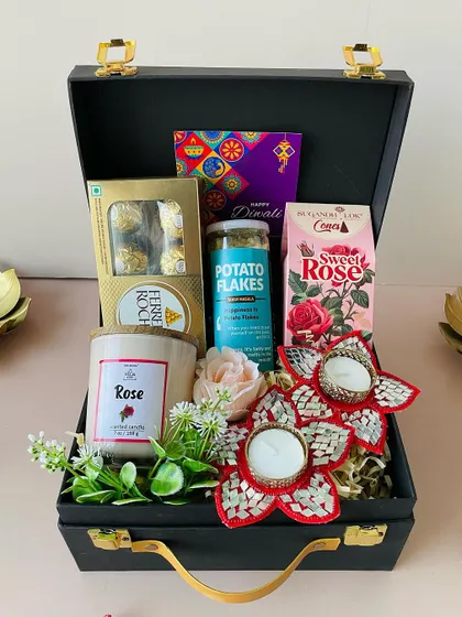 This black suitcase hamper is curated with a rose-scented candle, Ferrero Rocher chocolates, and festive mirror-work diyas, creating a luxurious sensory experience.