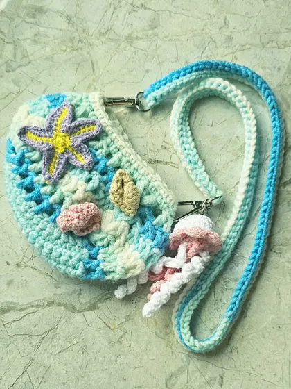 A detailed shot of the mini Ocean Bag, highlighting the different textures and colors of the seashell and starfish charms against the wavy blue and white pattern of the bag itself.
