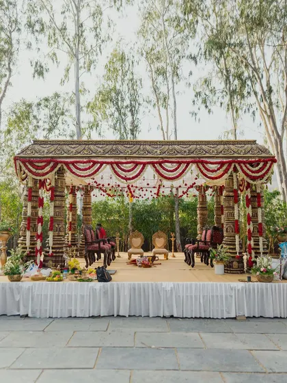 This outdoor mandap is a tribute to timeless South Indian temple architecture. The intricately carved pillars, traditional roof design, and garlands of red and white flowers create a sacred and majestic space for the wedding ceremony, beautifully integrated with the natural surroundings.