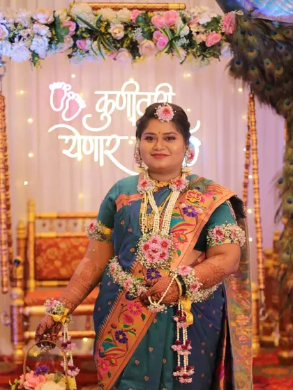 The mom-to-be looking radiant with our custom floral jewelry, standing in front of the decorated peacock theme jhula.