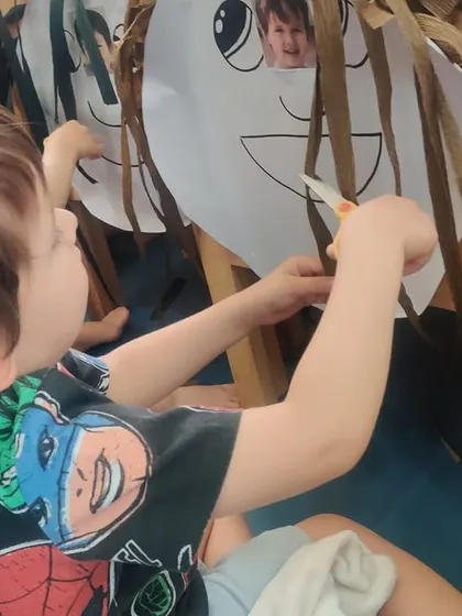 This boy is completely focused on his task of cutting the paper hair. Activities like this build concentration and fine motor control in a fun, imaginative context.
