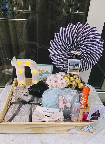 This personalized birthday tray includes a light-up initial 'D', a selection of clothing and accessories, Ferrero Rocher chocolates, and a mini polaroid for that extra personal touch.
