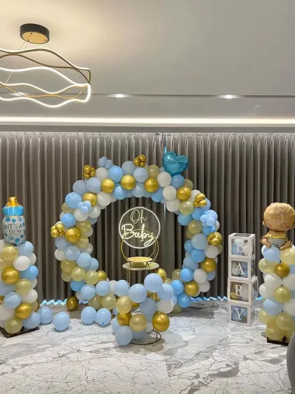 A beautiful "Oh Baby" setup for a home celebration. This full balloon ring in pastel blue, white, and gold creates a perfect photo corner, complete with balloon pillars and 'BABY' blocks.