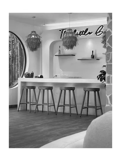 This monochrome image of 'The Little Bali' bar area focuses on the clean lines and composition of the space. The round window and textured pendant lights add visual interest against the minimalist backdrop.