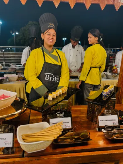 A smiling chef from my sushi team, presenting freshly made rolls at her station.