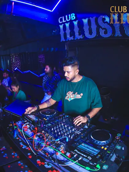 A focused moment at the decks at Club Illusions, with the club's signature blue lighting setting the mood.