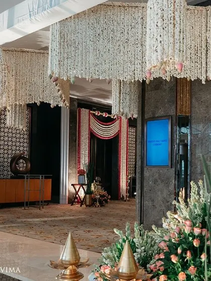 The entrance to a half-saree ceremony, adorned with fragrant jasmine garlands and banana leaves. The reflection on the polished floor doubles the beauty of this traditional South Indian decor.
