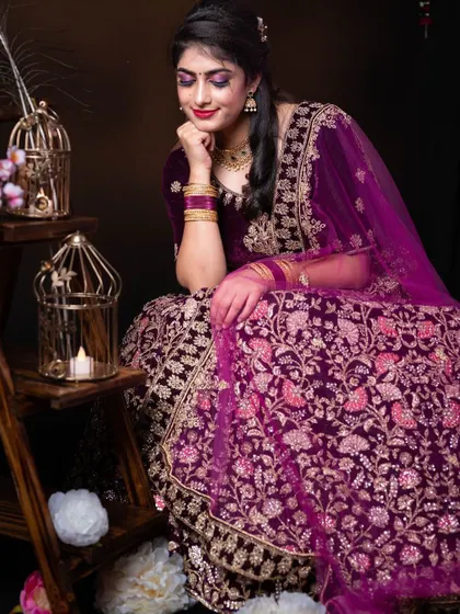 A seated portrait of a client in our purple velvet lehenga, showcasing the intricate embroidery details.
