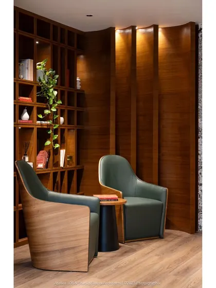 Another angle of the reading area, showing how the wooden shelving flows onto the adjacent wall in vertical, subtly bent elements. This detail adds a dynamic and sculptural quality to the warm and inviting space.