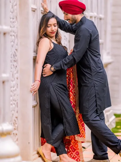 A romantic pose against a backdrop of white pillars. The couple's all-black traditional outfits with a pop of color from the dupatta create a very stylish look.