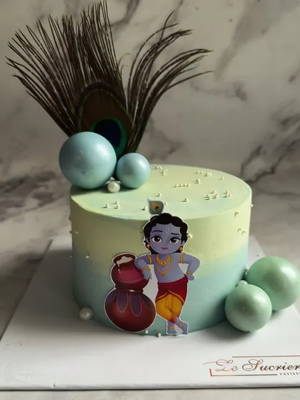 Celebrating Janmashtami the sweetest way. This cake features a serene blue and green gradient, adorned with a peacock feather and a charming illustration of Little Krishna.