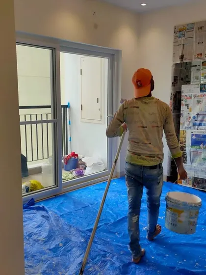A clean workspace is a priority. This painter is walking across a protected floor, with blue tarpaulin covering the entire area, ready to apply a fresh coat to the walls of this apartment.