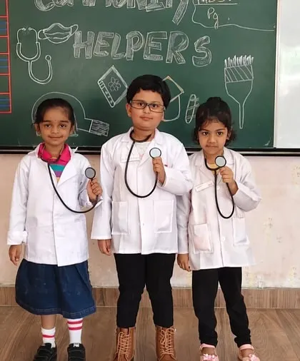 Our little doctors are in! Three students dressed in white coats with stethoscopes, ready to learn about the medical profession during our Community Helpers activity.