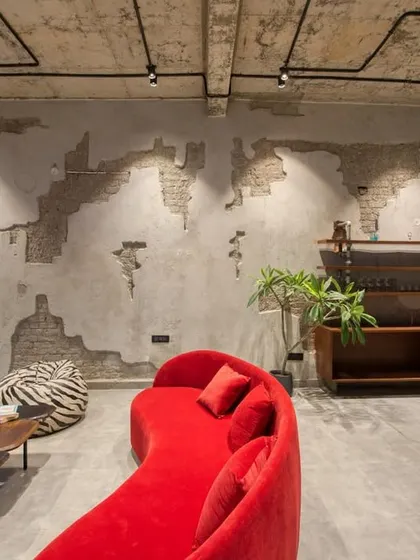 This industrial-style lounge area features exposed brick and concrete walls, a bright red curved sofa, and a foosball table, creating a fun and edgy entertainment space.