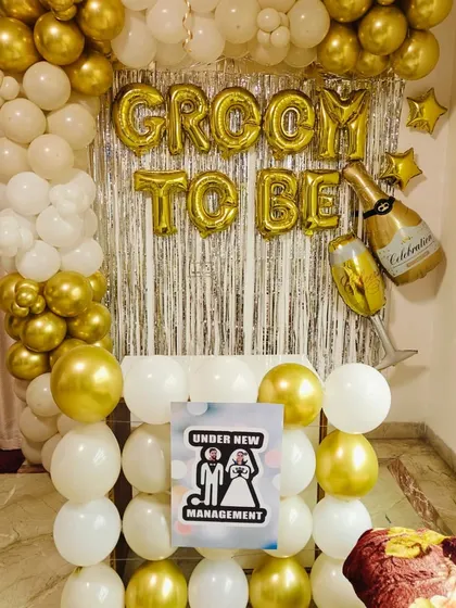 A fun "Under New Management" sign for a groom-to-be party. This setup features a classic gold and white balloon backdrop.