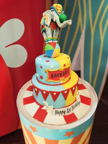 This circus-themed cake is a feast for the eyes, with a balancing elephant, colorful flags, and a classic red and yellow color scheme. It’s perfect for a fun-filled first birthday party.
