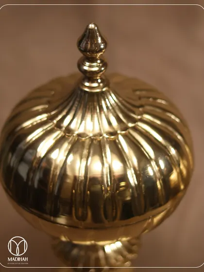 A close-up of the Mughal Gold Jar, highlighting the detailed fluting on the lid and the warm, reflective glow of the polished brass. It's a piece that speaks of heritage and craftsmanship.