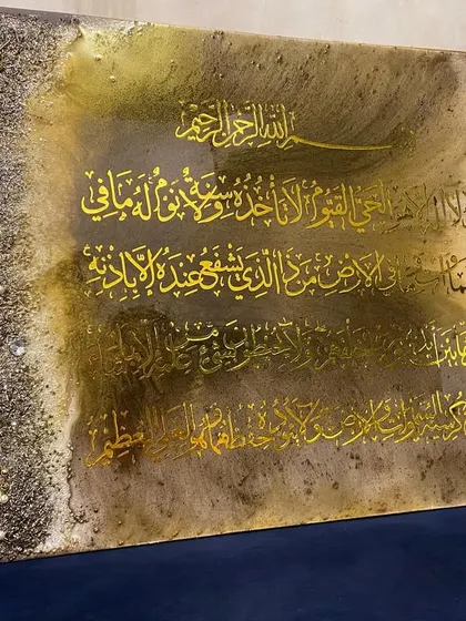 Another view of the large brown and gold Ayat al-Kursi artwork, placed on a blue sofa to highlight its colors.