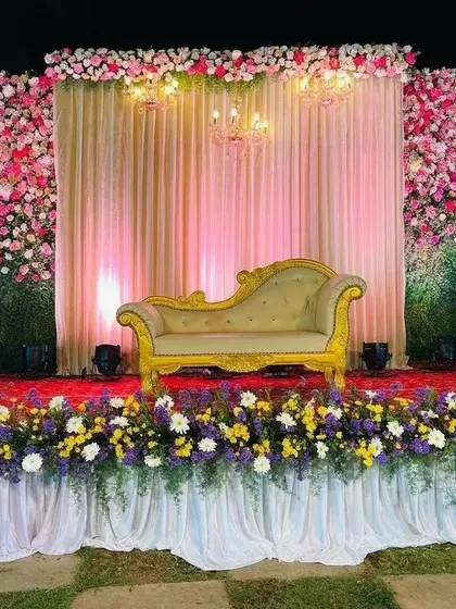 This stunning reception stage features a massive wall of pink and white flowers, creating a luxurious and romantic backdrop. The stage is lined with a mix of colorful blooms, perfect for a grand celebration.