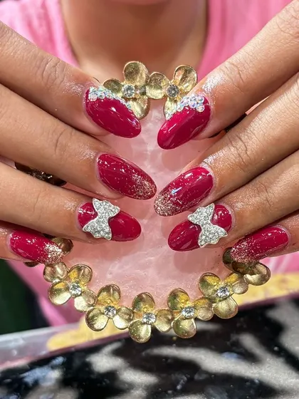 Rich maroon nails decorated with sparkling silver bows and a gold glitter gradient for a luxurious finish.