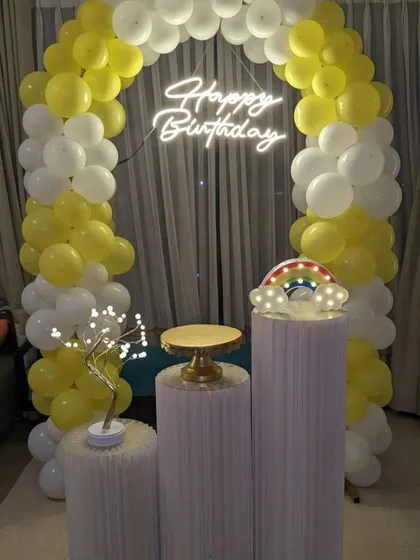 A minimalist birthday setup with a yellow and white balloon arch and a neon sign, perfect for a clean and modern look.